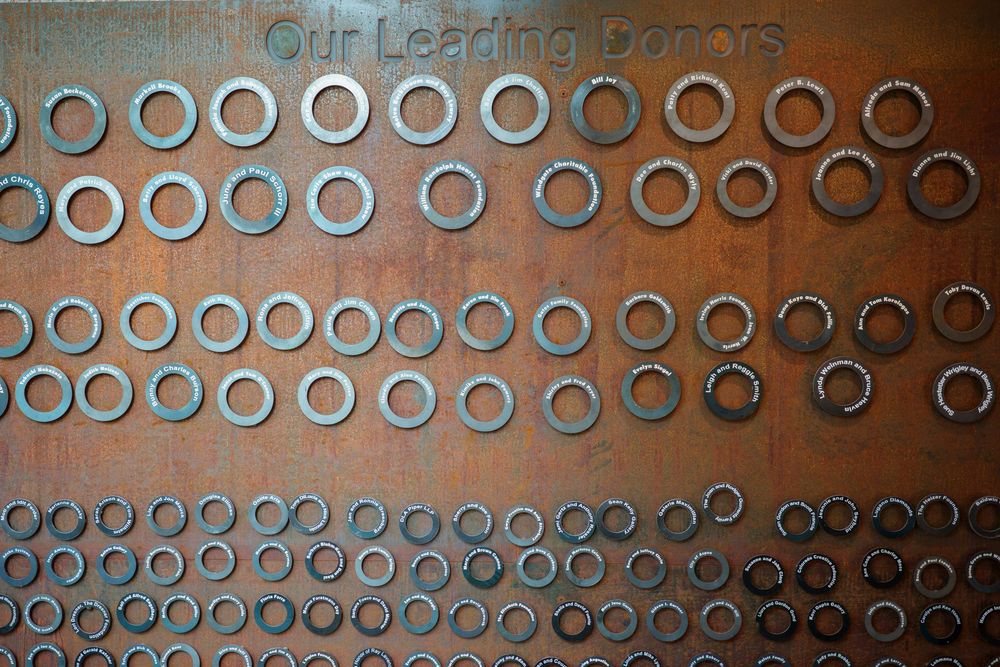 Metal donor recognition wall featuring rows of circular rings on a textured bronze surface.