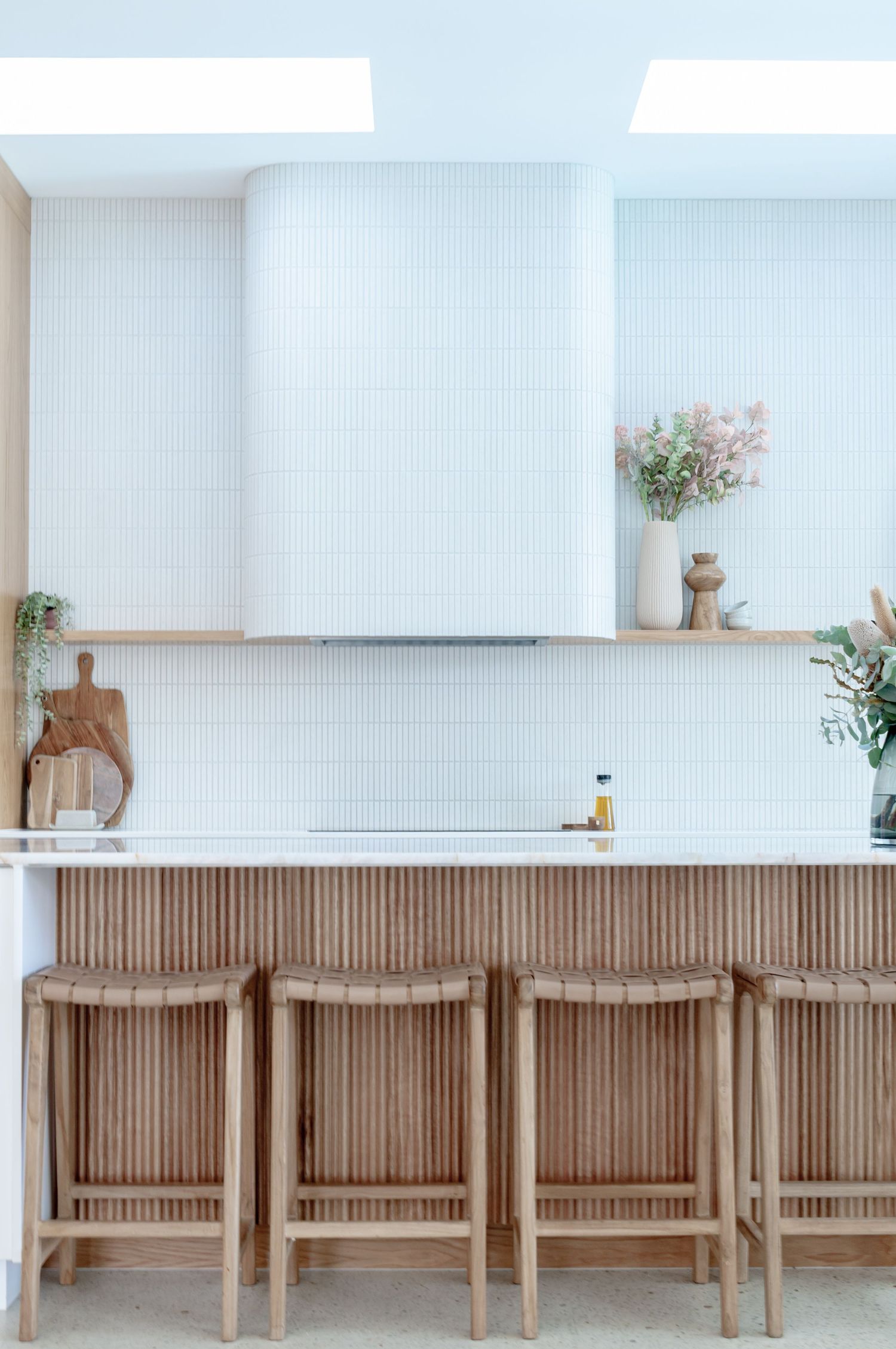 Modern white and wood kitchen features a minimalist island with bar seating and natural lighting from skylights.