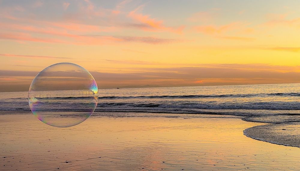 Transparent bubble reflects sunset colors over ocean waves on a sandy beach.