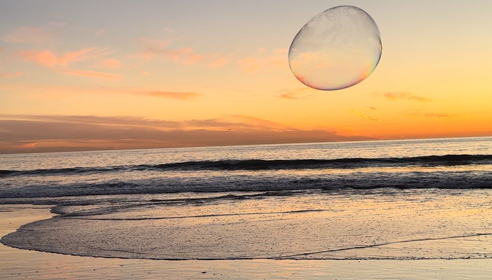 Large bubble floating over a beach at sunset with golden sky and waves.