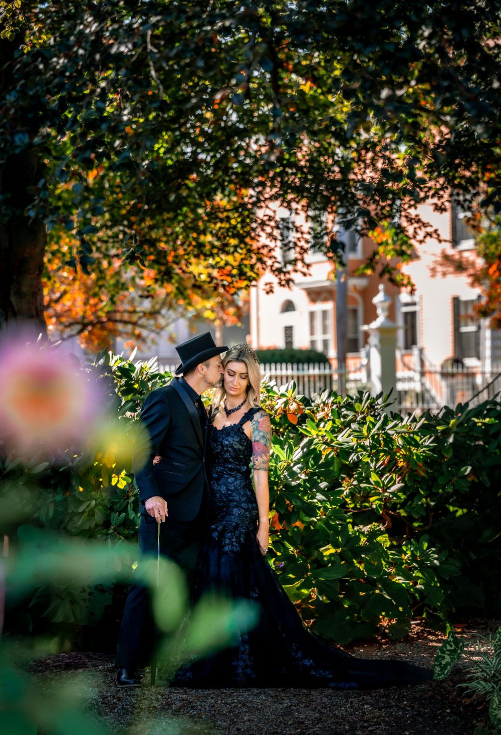 A romantic couple poses under autumn trees in a garden setting during a golden sunset photo session.