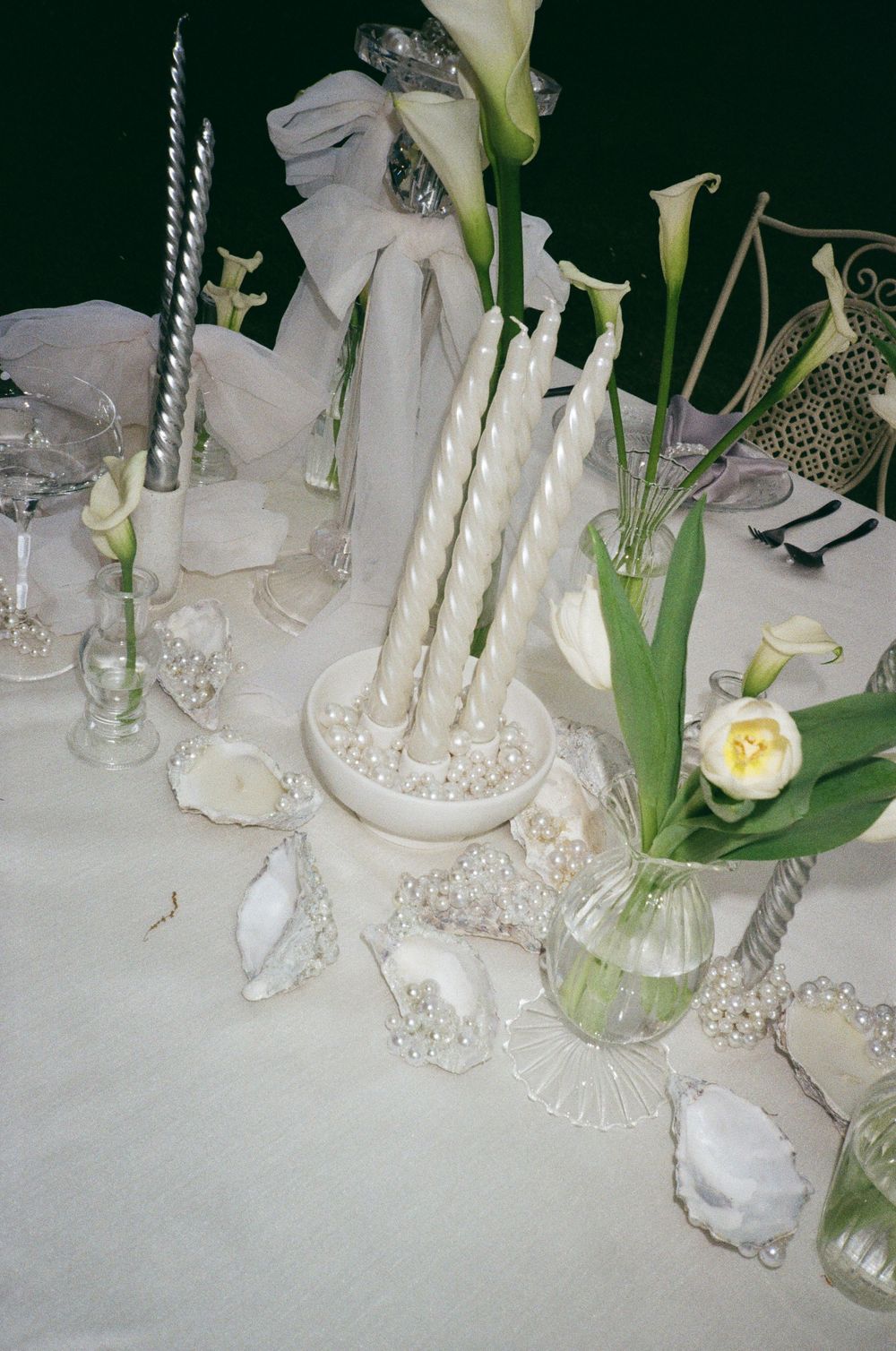 Elegant white floral wedding table decor with candles, crystal glassware and delicate arrangements on a white tablecloth.
