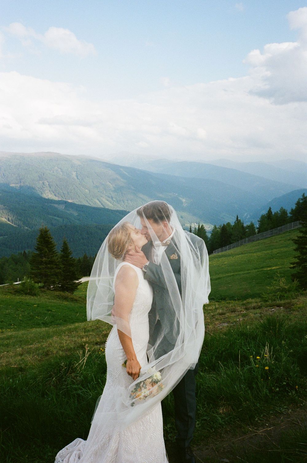 Mountain top wedding portrait with flowing veil against dramatic alpine landscape.