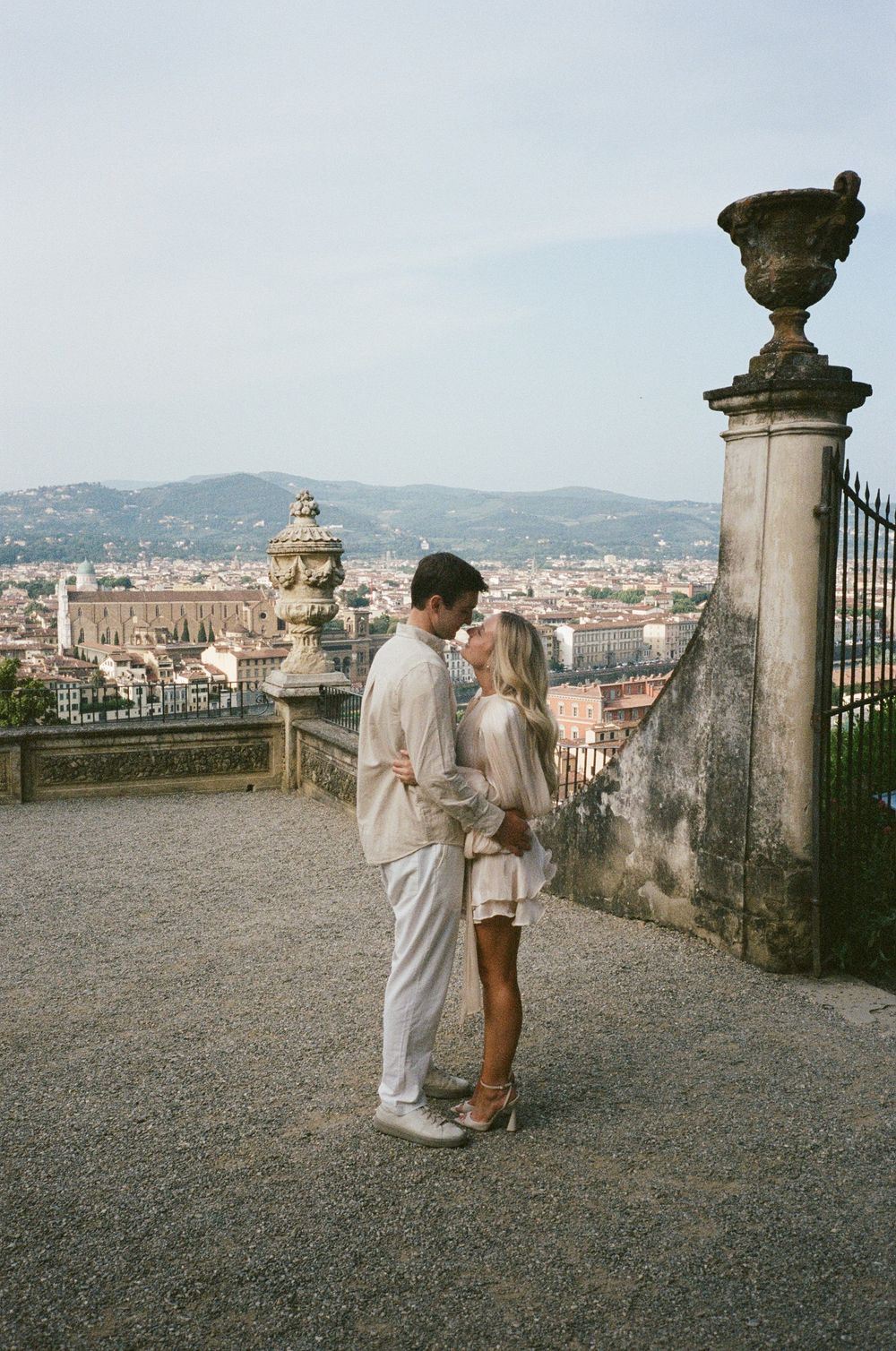 Romantic couple in light colored outfits sharing a moment at a scenic overlook of Florence, Italy.