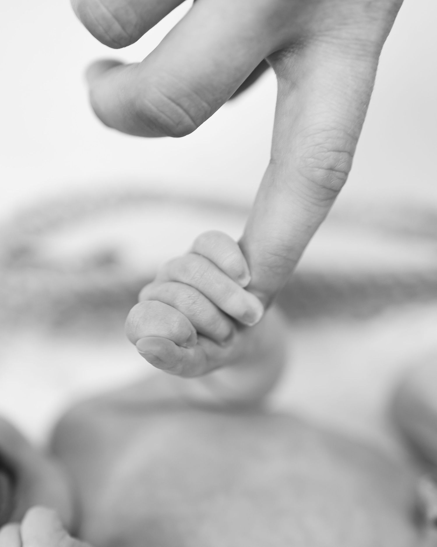 Baby's small hand gently touches an adult finger in a tender black and white moment of connection.