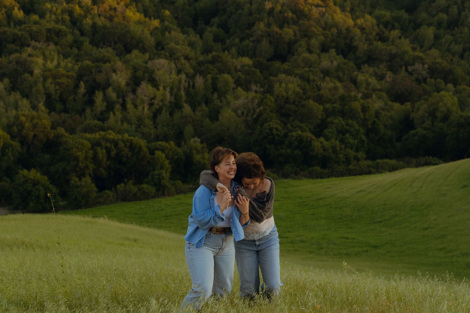 m/f couple in the field - her arms draped over the his shoulders and leaning forward onto him.