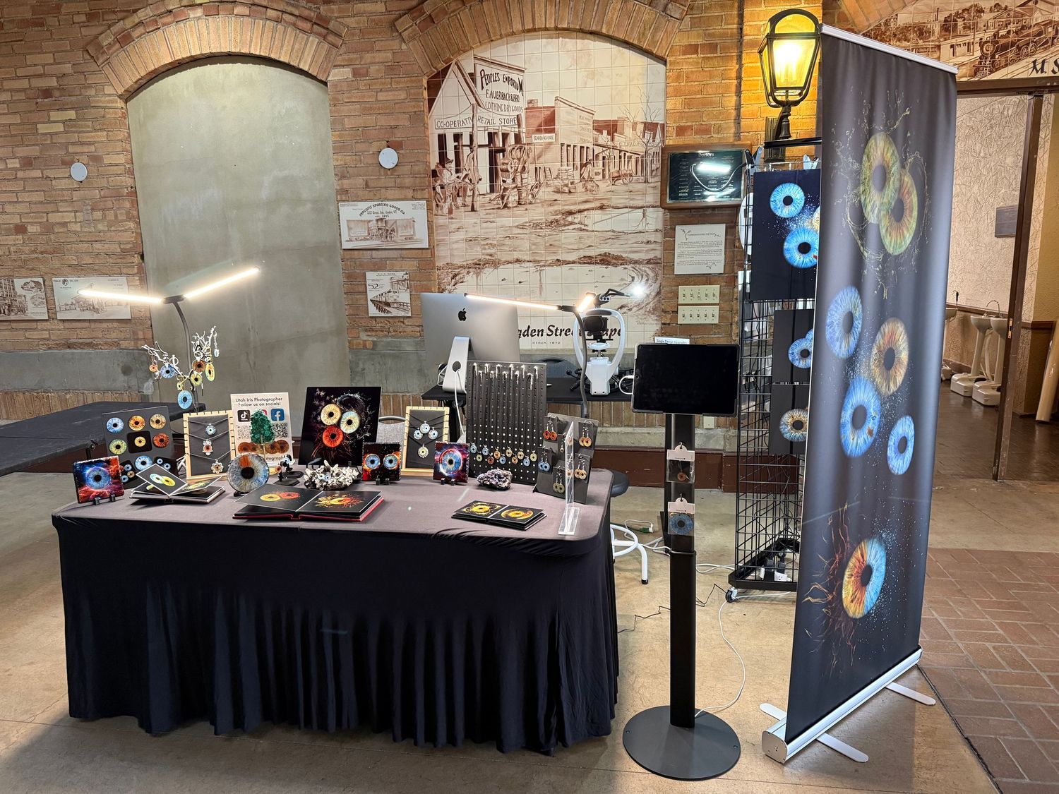 Merchandise display table with black tablecloth and retractable banner stand in brick-walled venue space.