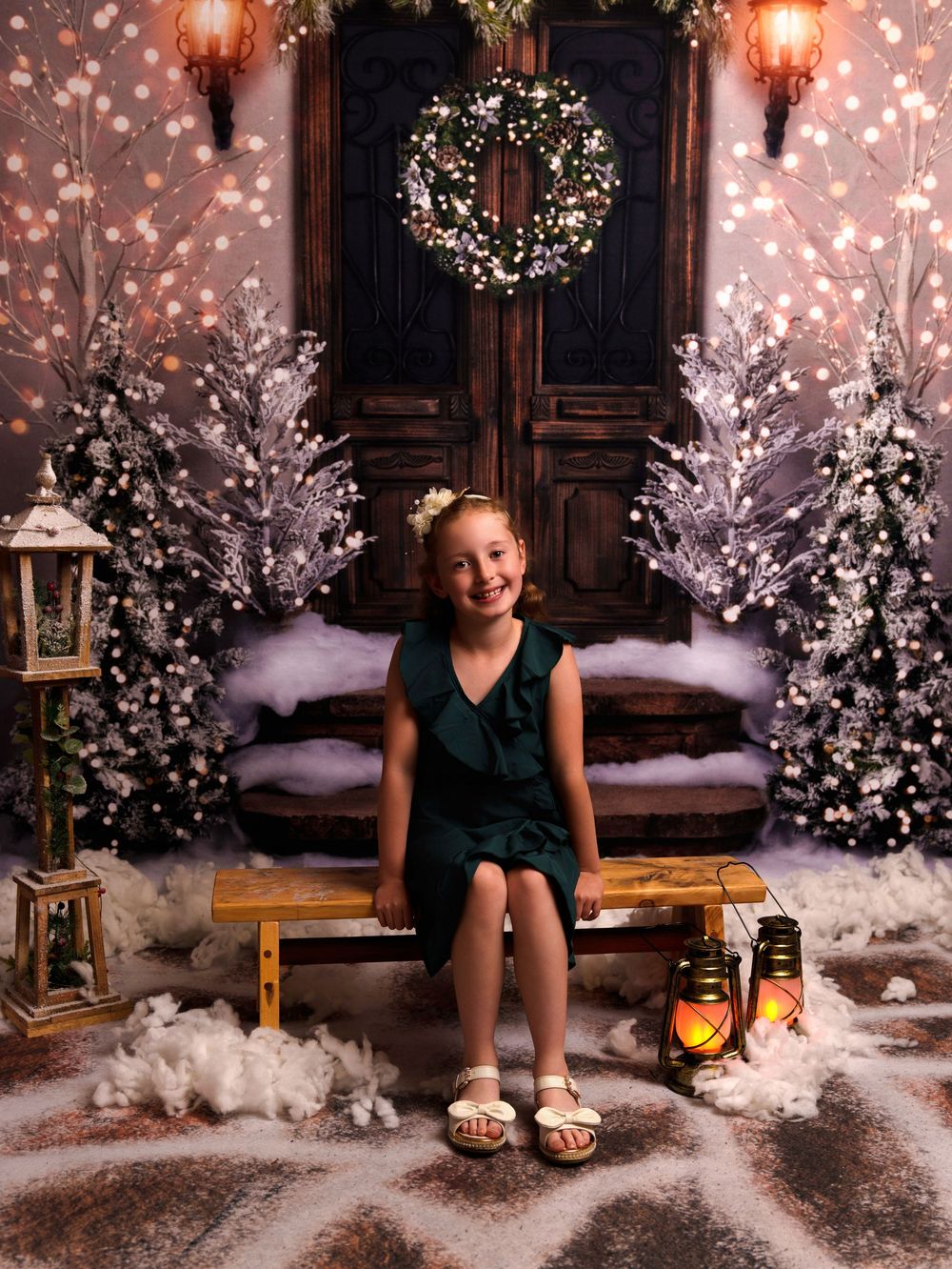 Christmas scene with frosted trees, wreath on wooden doors, lanterns and cozy wooden bench decorated with soft white snow.