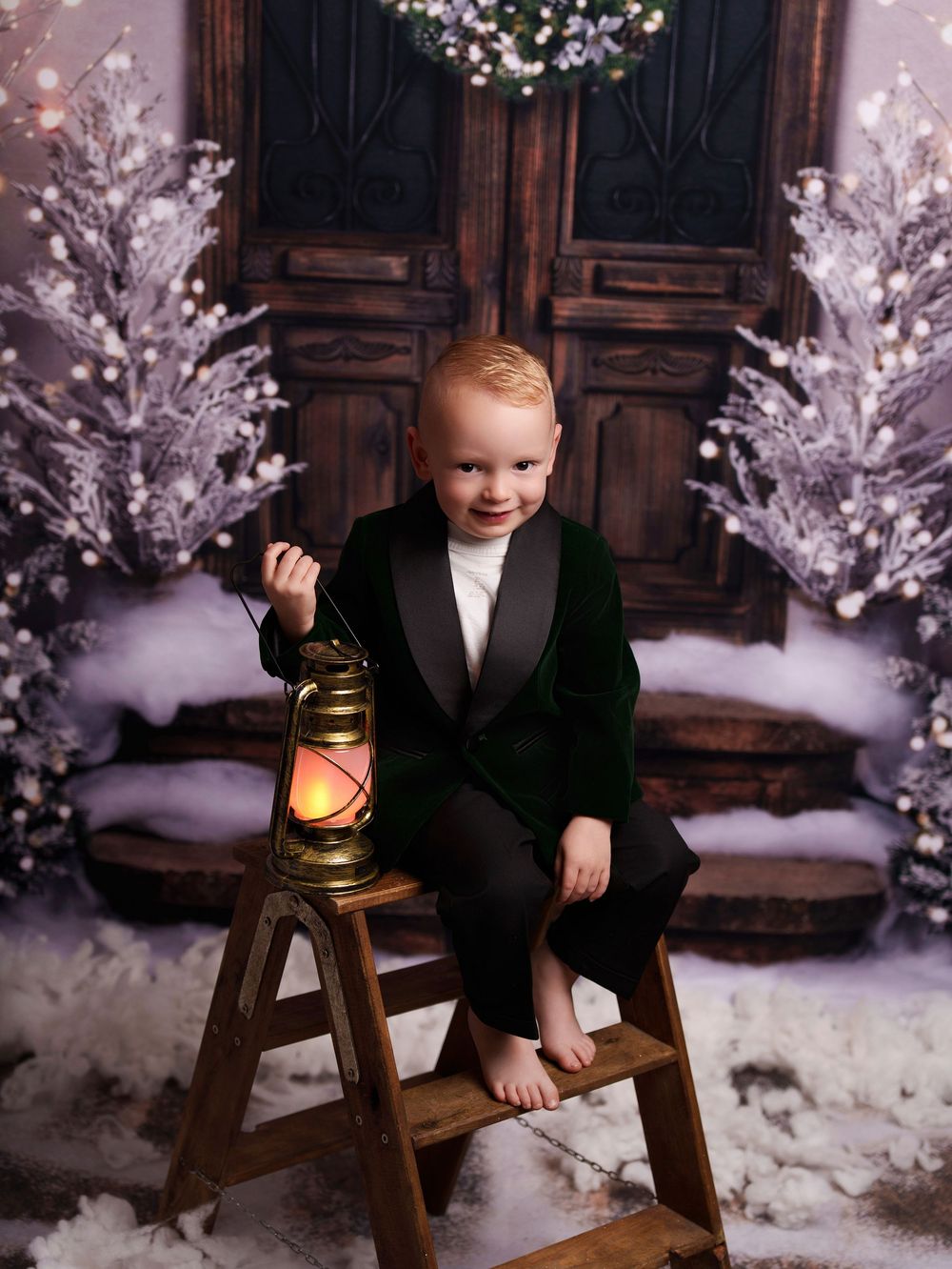 A winter holiday photo session featuring a wooden chair and snowy white trees with twinkling lights in the background.
