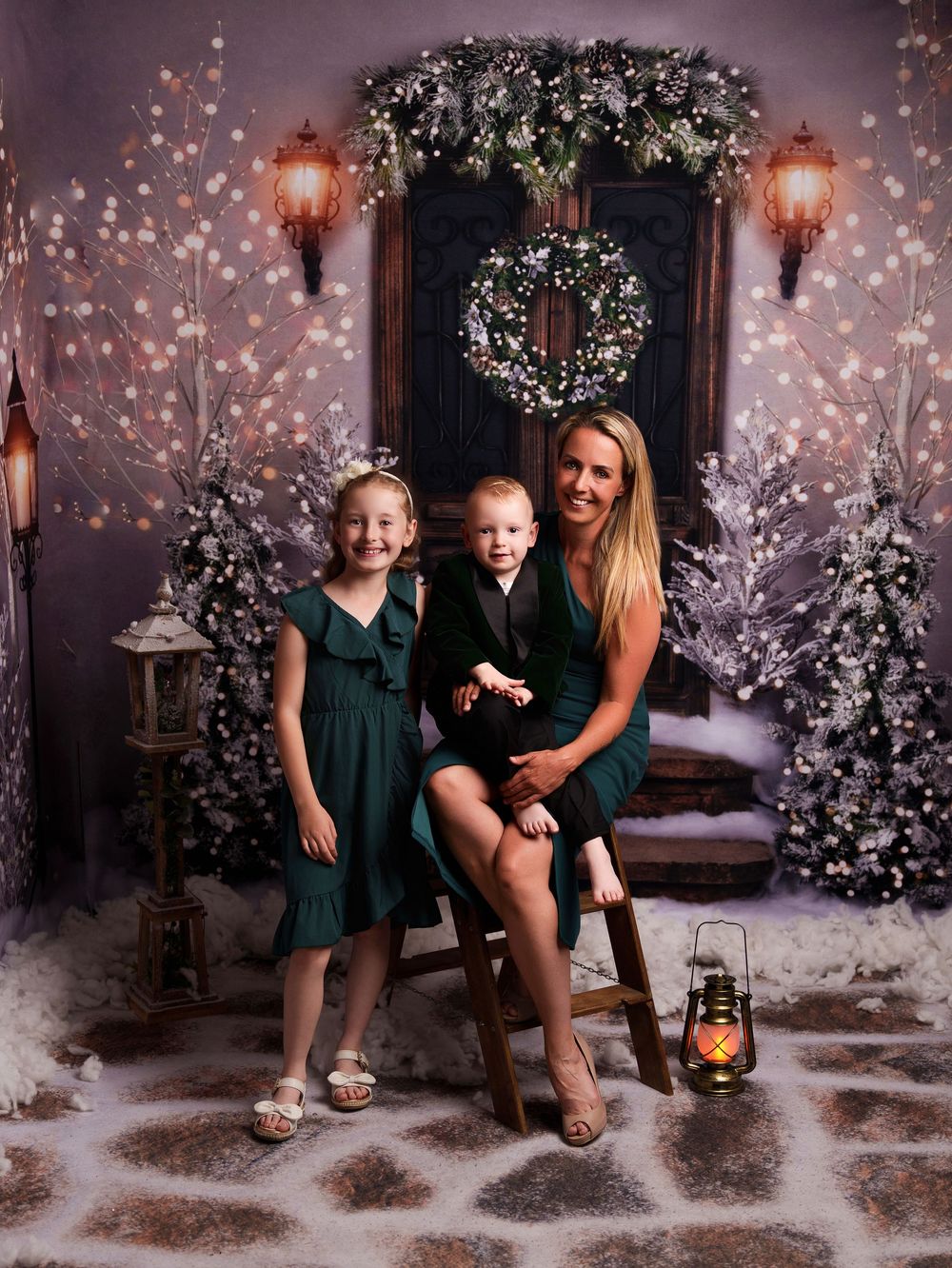 Family portrait in front of decorated Christmas trees with lantern and snowy backdrop.