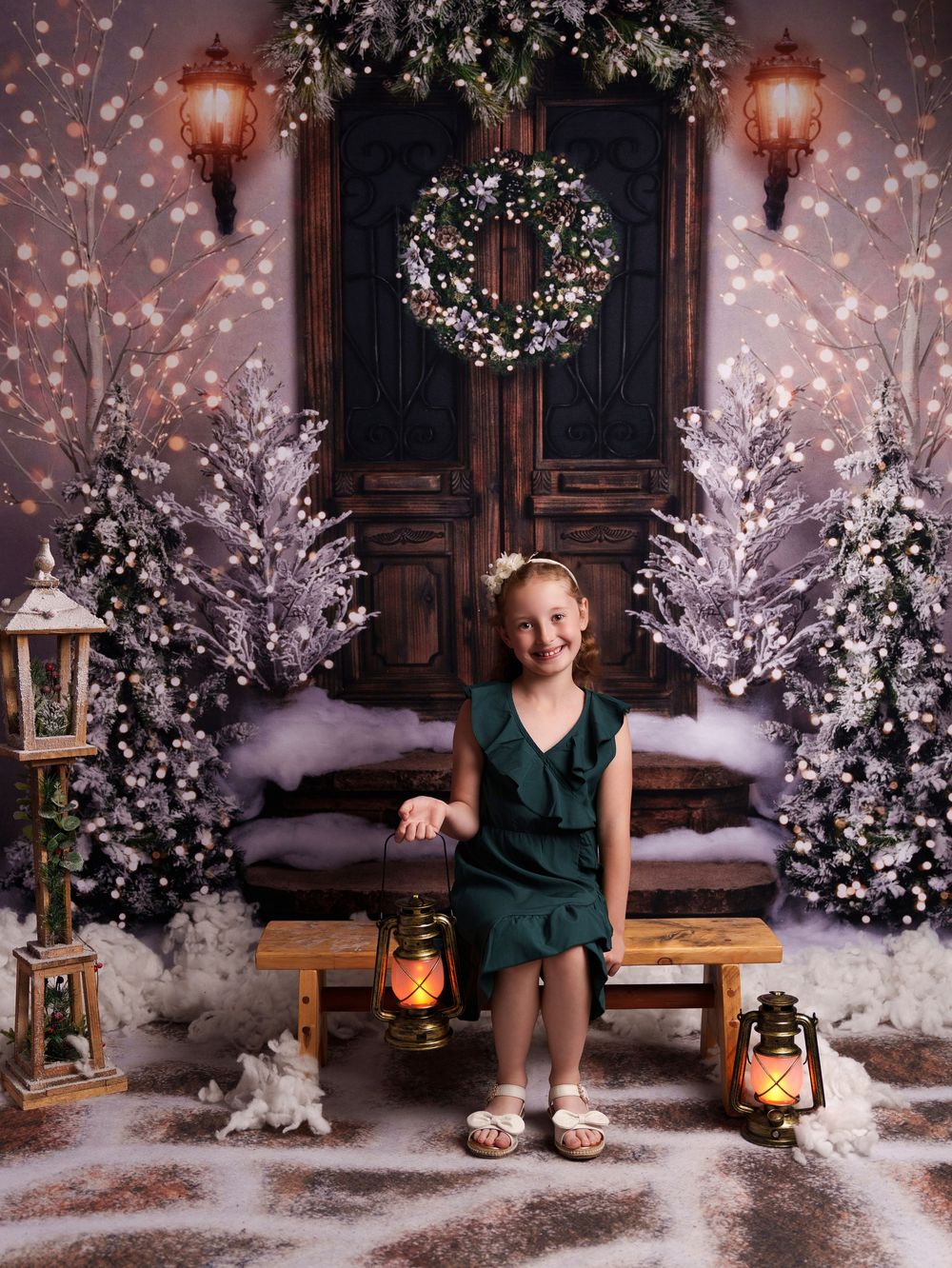 A winter wonderland photo setup with white trees, lanterns, and a wooden bench against a dark backdrop.