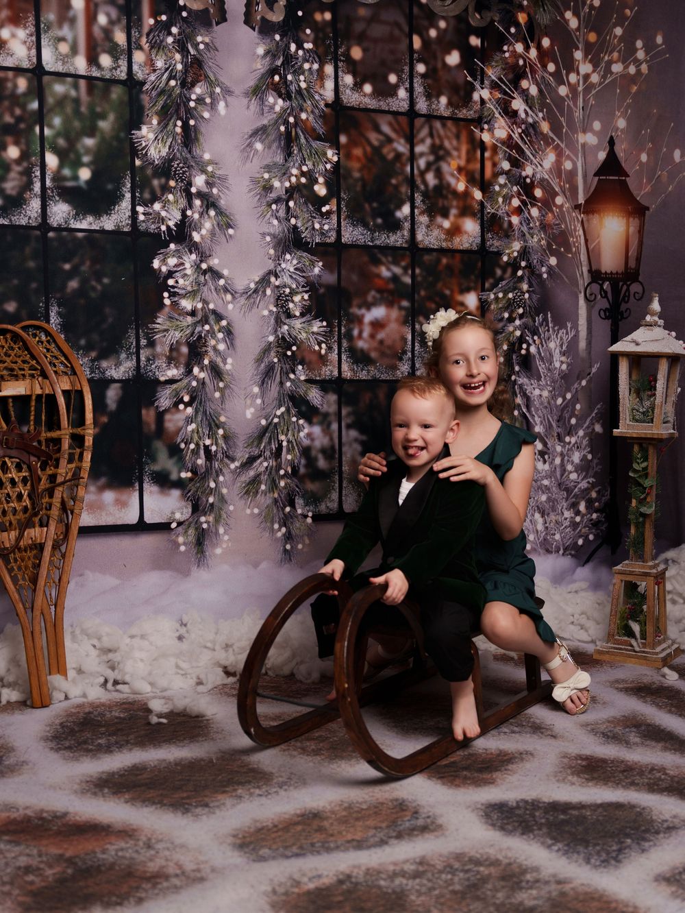A child plays in a magical winter scene with snow, twinkle lights and vintage decor in a photo studio setting.