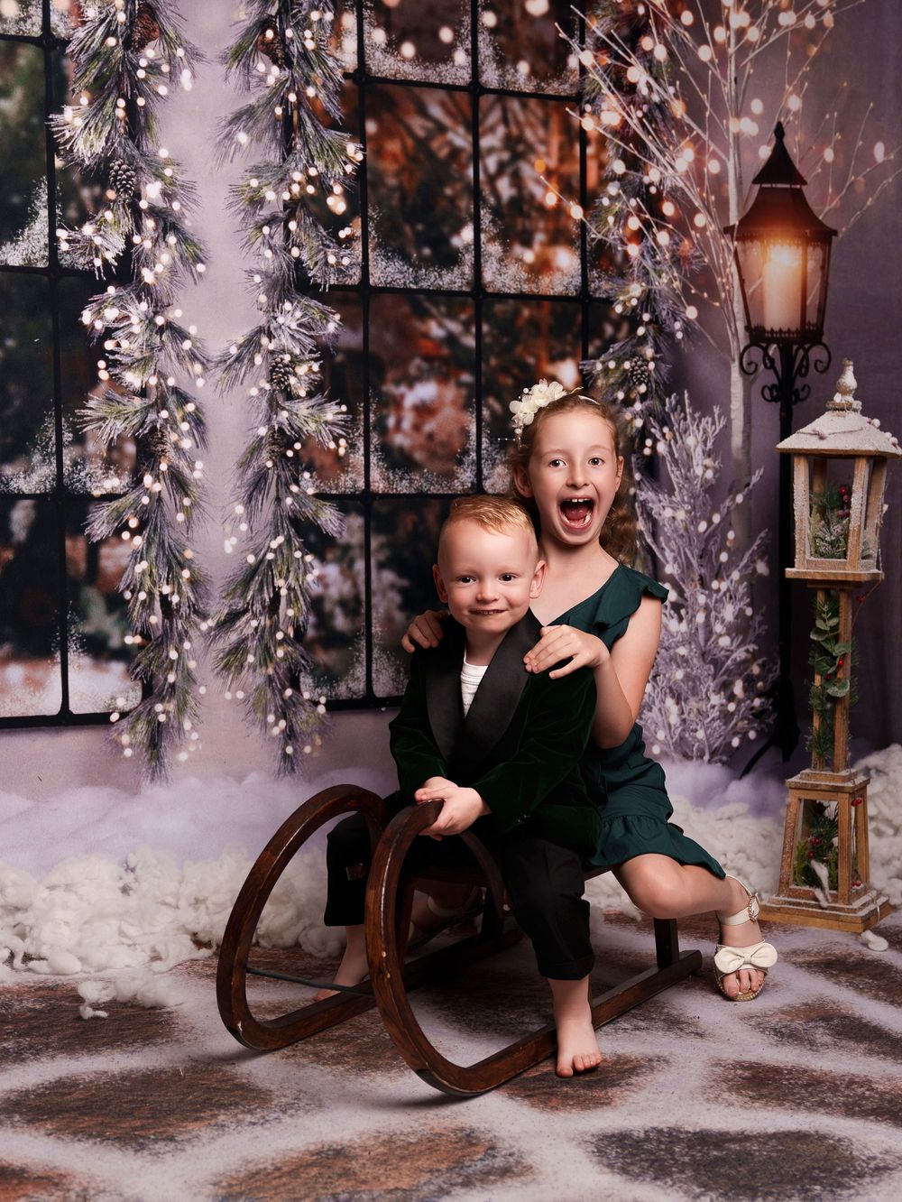Children pose in a winter wonderland studio setting with lanterns, snowy trees, and rustic decor.