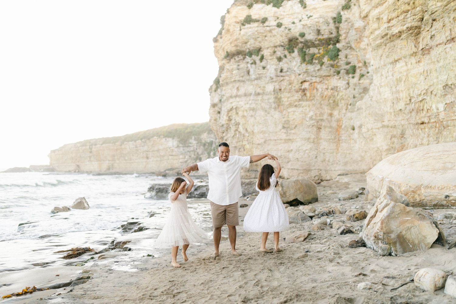 People in white outfits walk along a beach with steep limestone cliffs towering behind them at sunset.