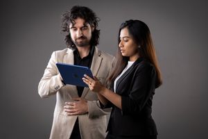 Professional couple in business attire interact with a document and mobile device in a gray studio setting.