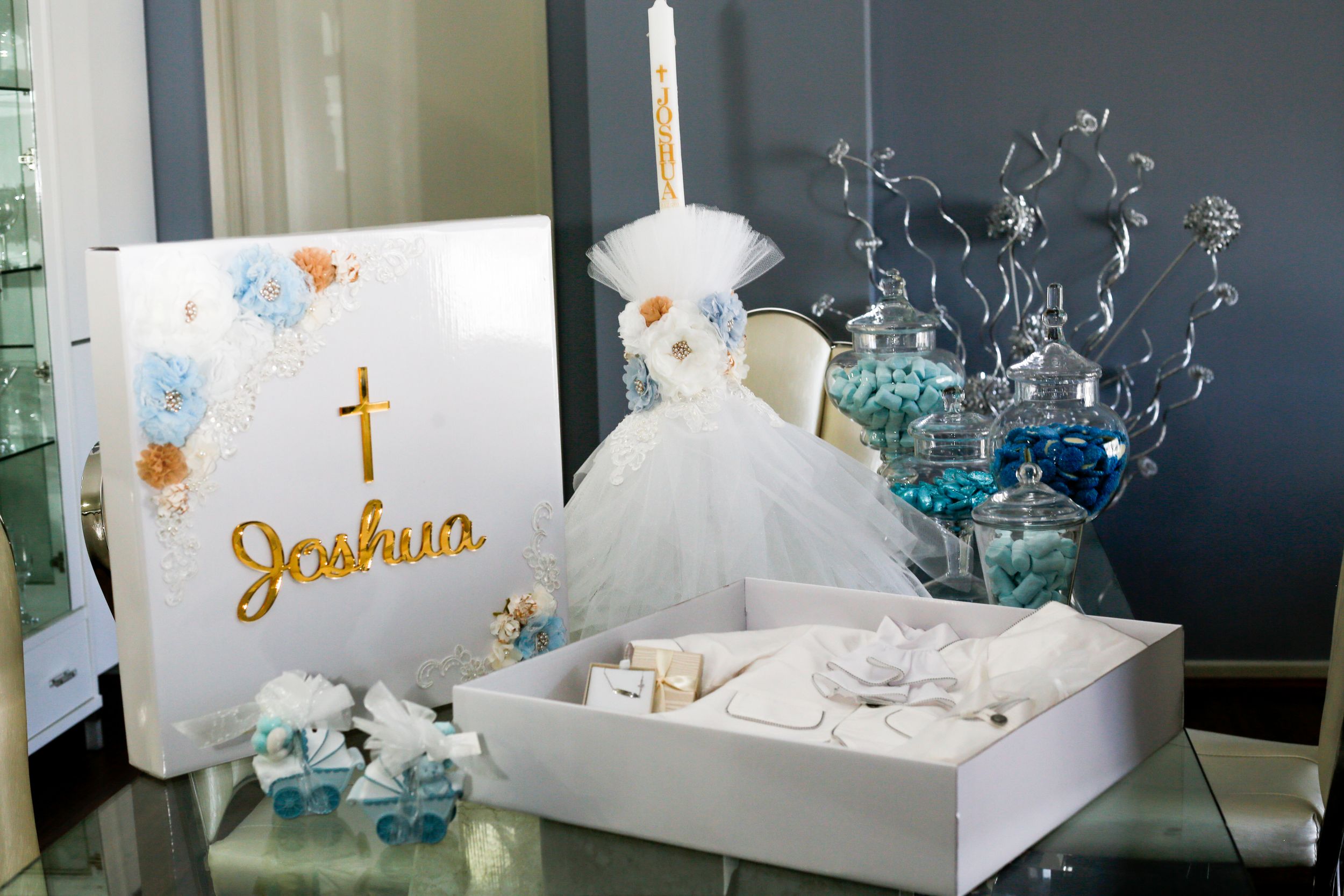 Elegant baptism party decorations with white dress, cross, and blue accents.