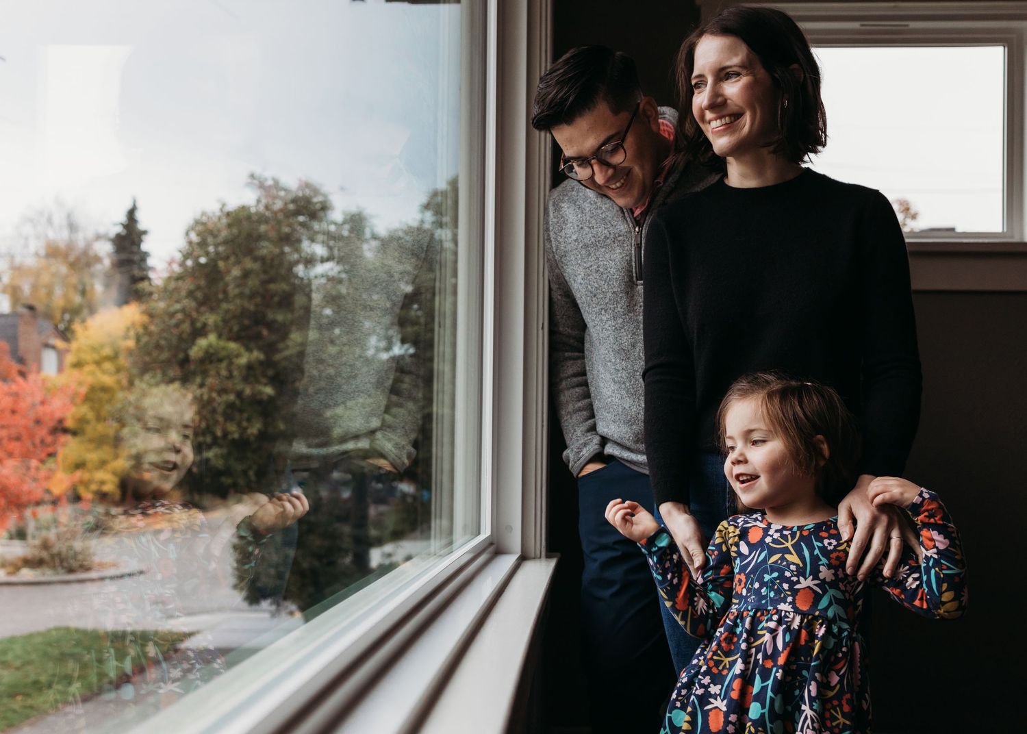 A loving family shares a joyful moment looking out their window together at autumn foliage.