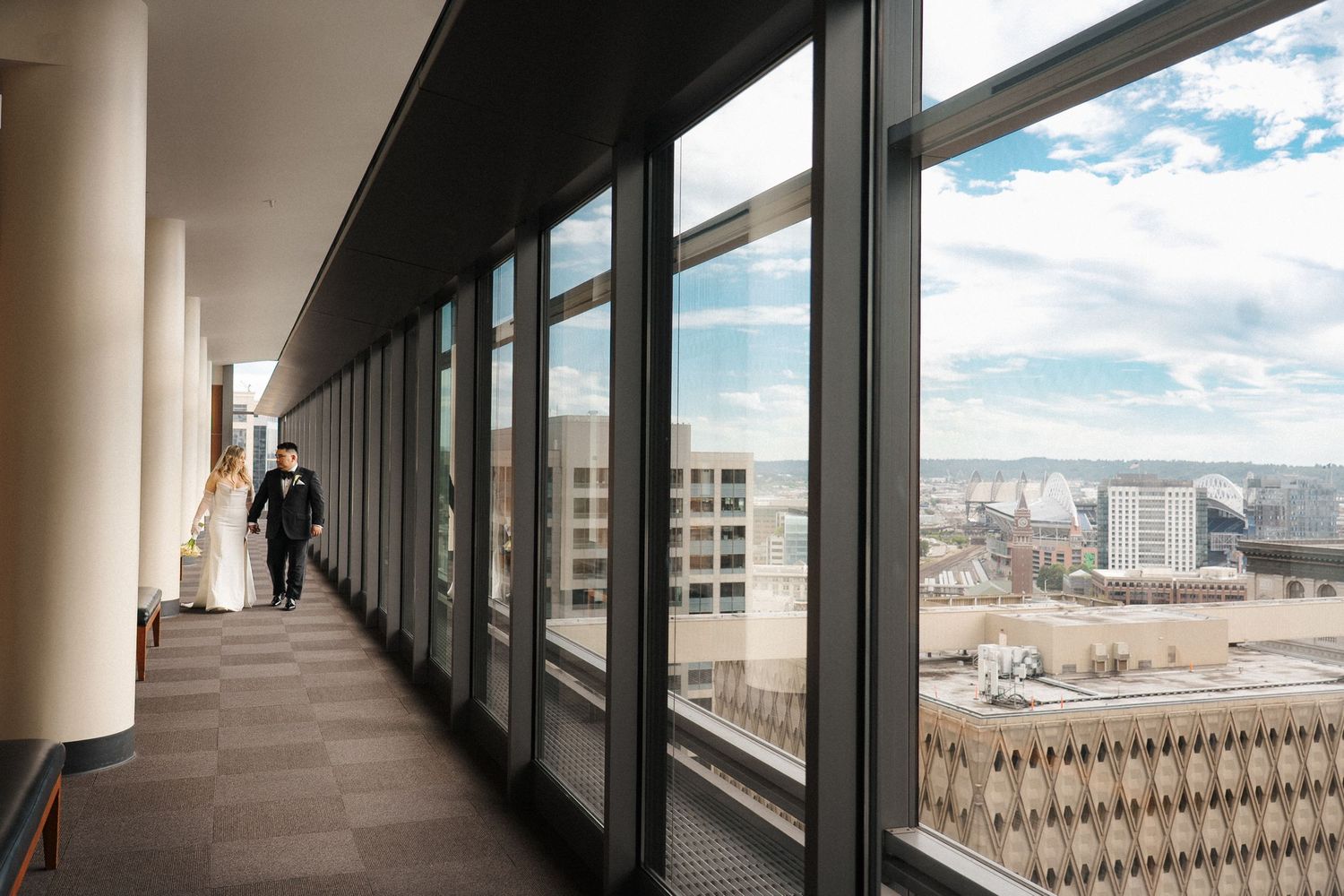 Modern office hallway with floor-to-ceiling windows overlooking a cityscape on a partly cloudy day.