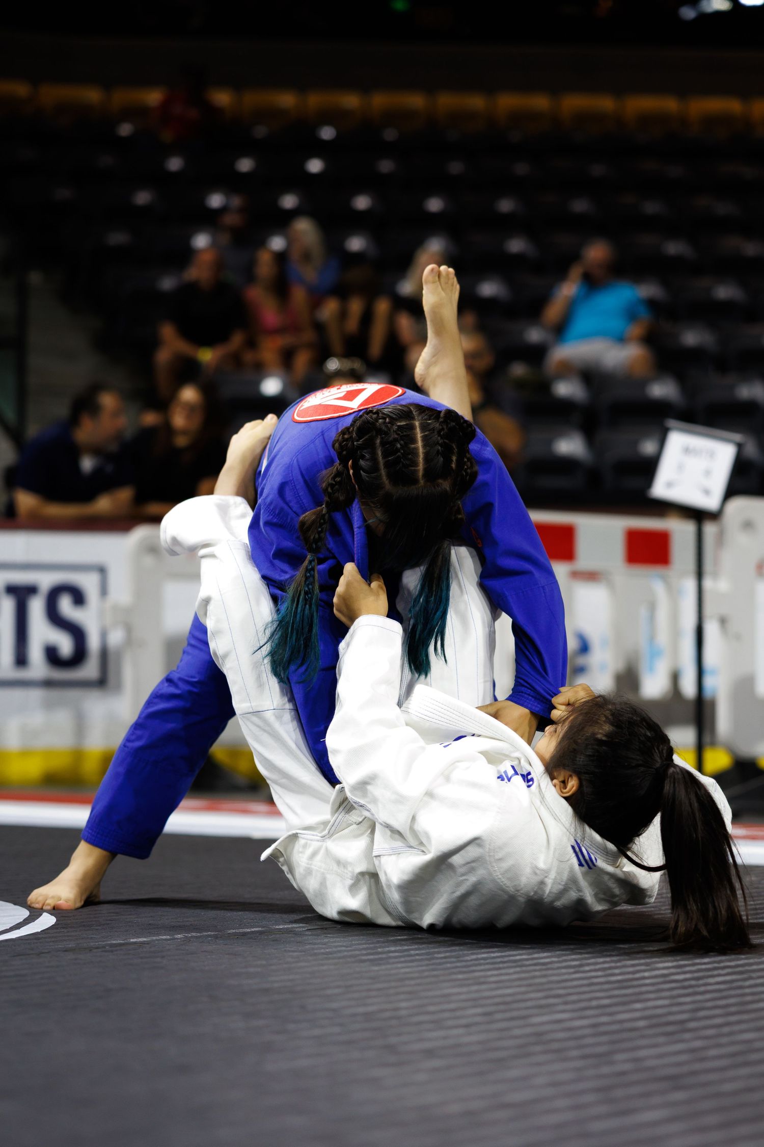 Martial artists in white and blue gis practicing ground techniques during a competition.