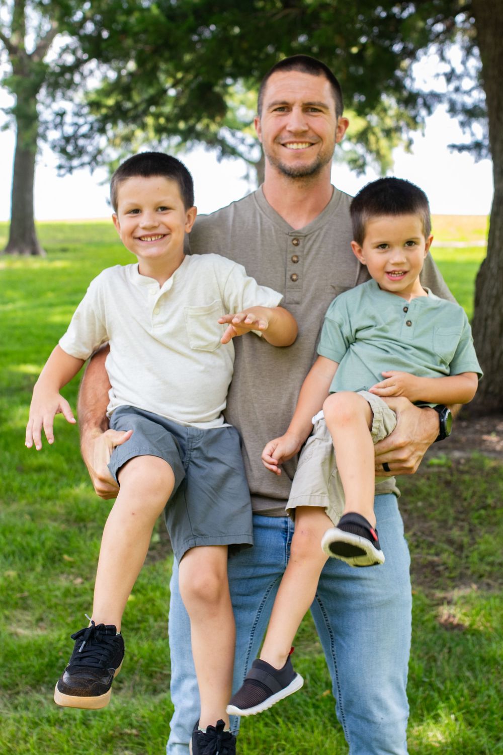 Playful family moment captured on green grass under trees.