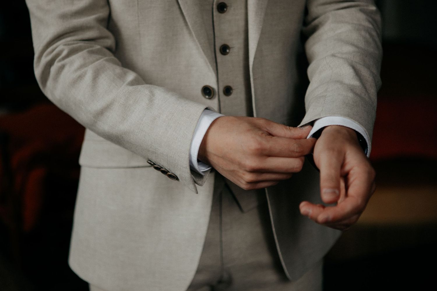 Groom in a beige three-piece suit adjusting his cufflinks before the wedding.
