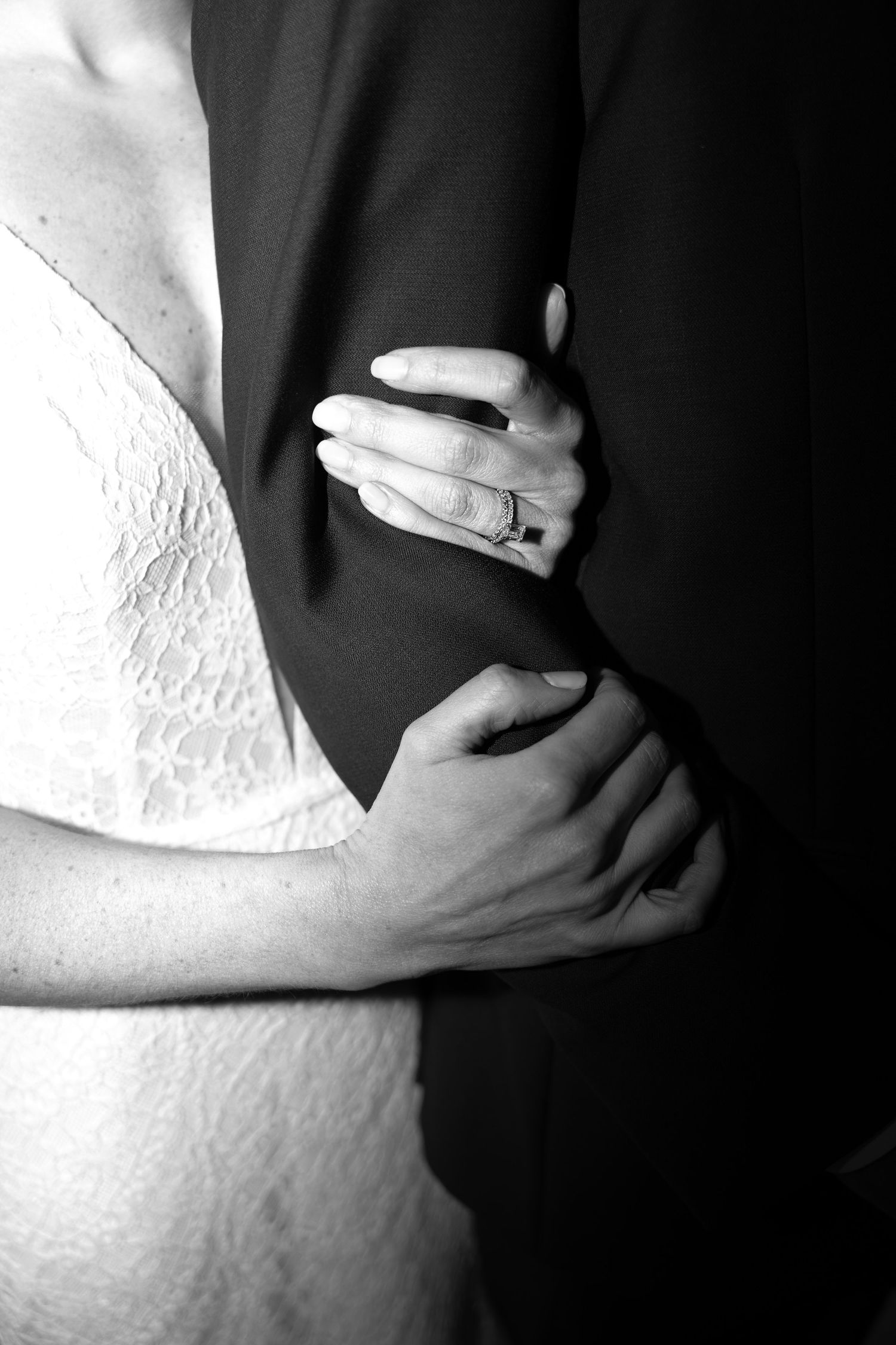 Black and white wedding photo showing close up of embracing couple with wedding ring visible on hand.