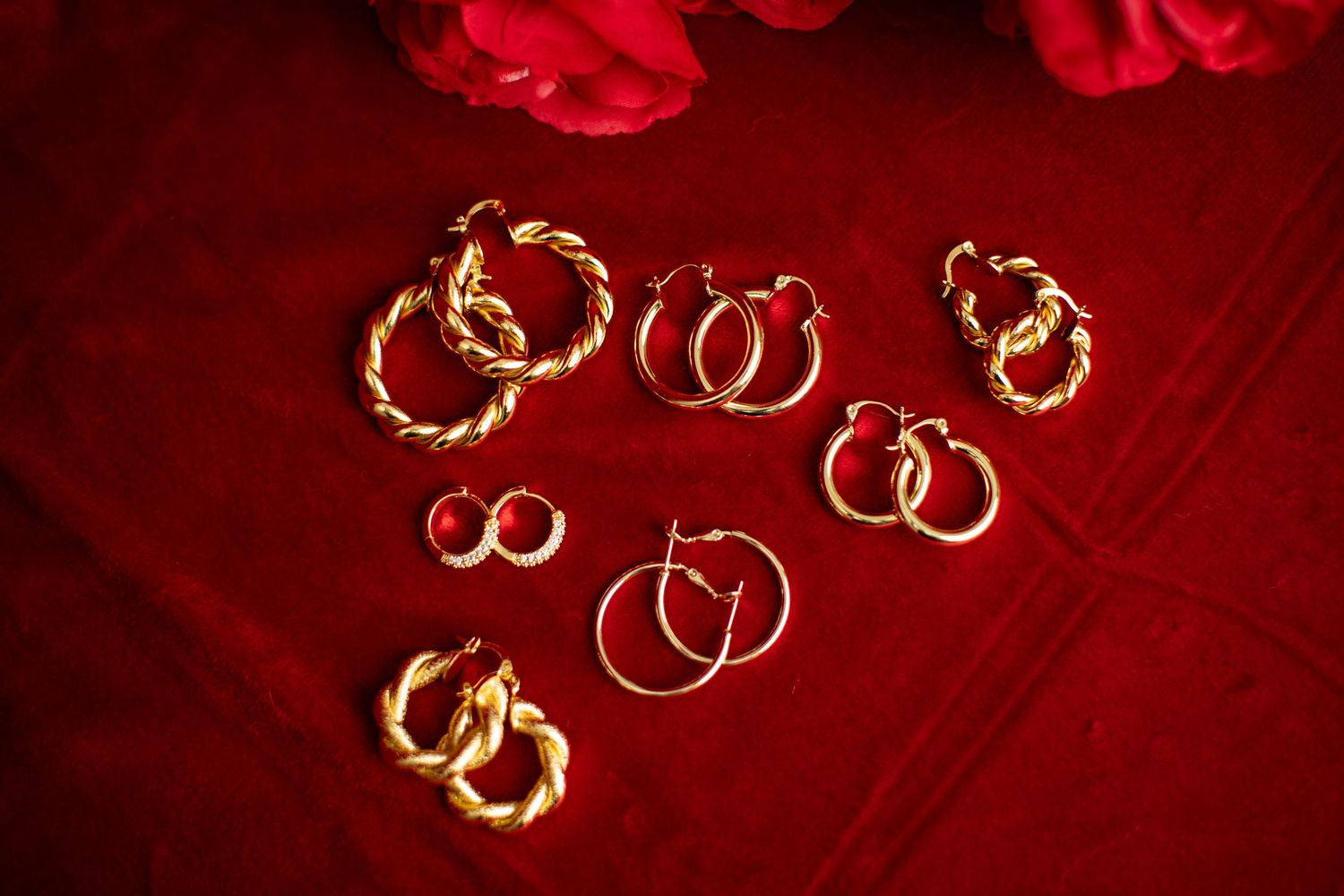Several pairs of gold hoop earrings displayed on a luxurious red velvet background.