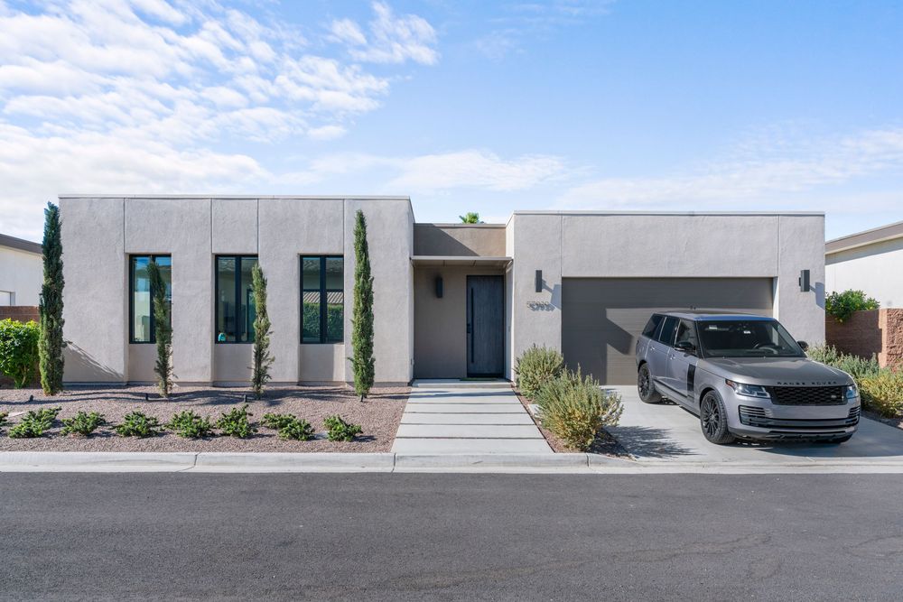 Modern white single-story home with sleek architecture, tall windows, landscaped front yard, and covered carport in suburban setting.