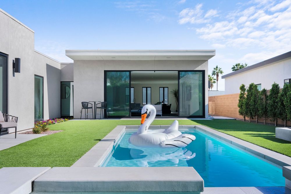 Modern luxury home exterior with swimming pool, artificial turf lawn and white inflatable pool float in backyard.