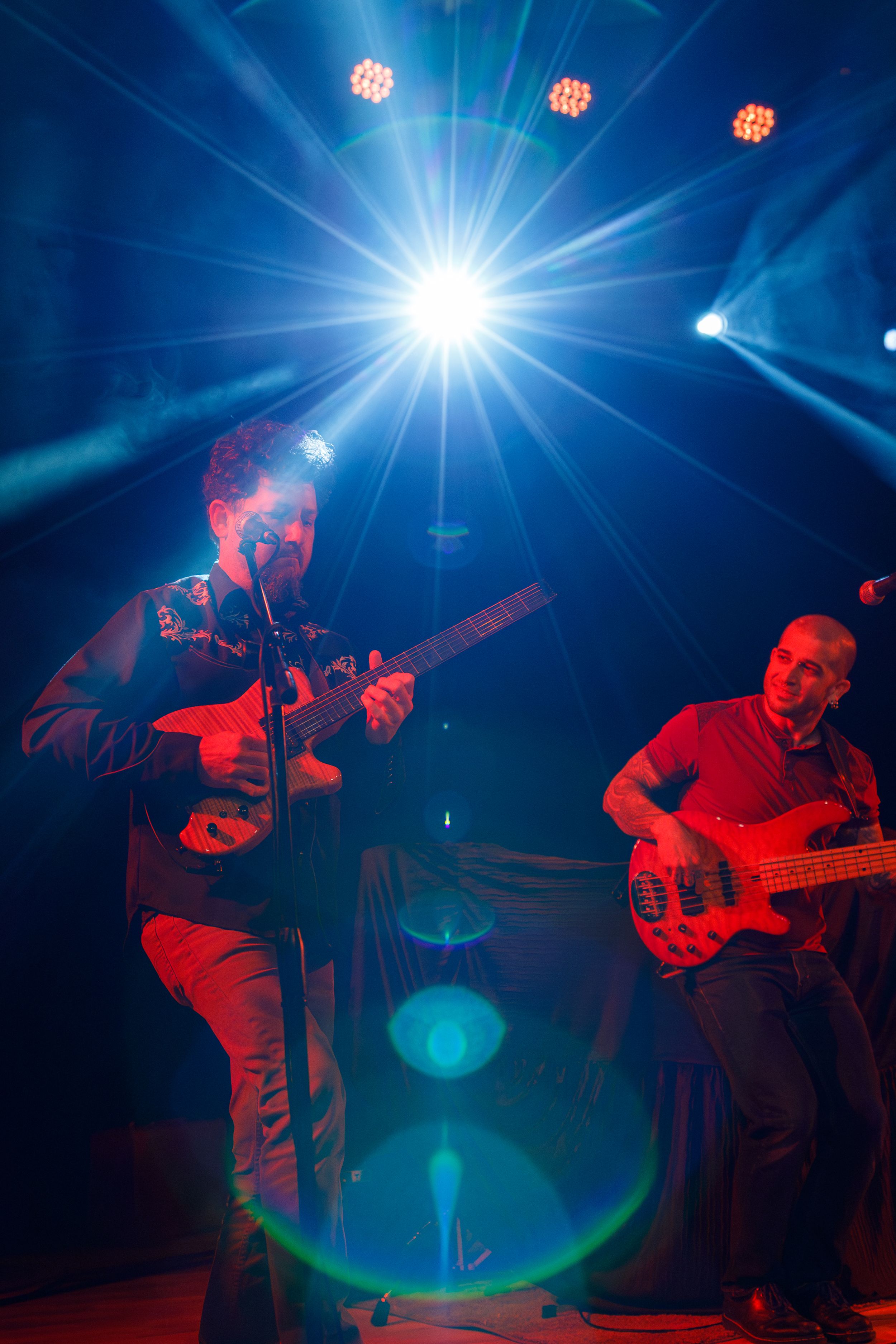 Musicians perform on stage with dramatic blue stage lighting and starburst effect creating an atmospheric concert scene.