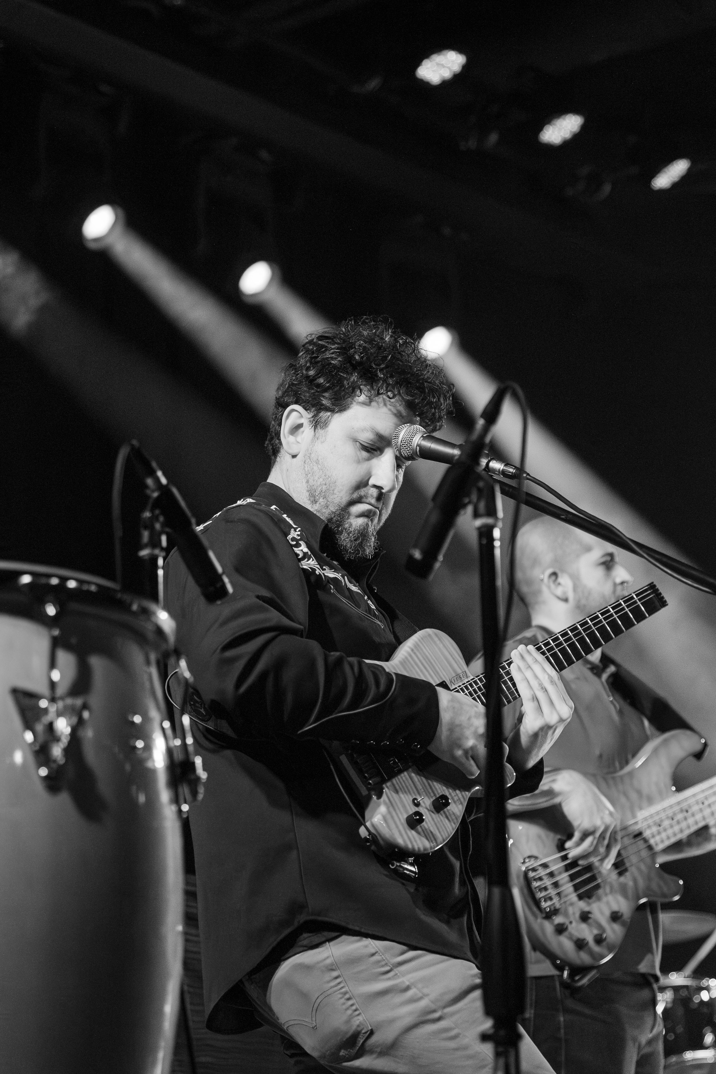 Black and white photo of guitarist performing on stage with dramatic lighting and a bass player in the background.