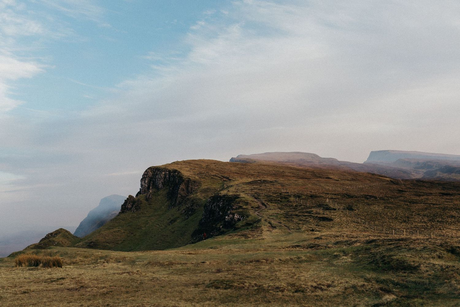 Dramatic cliffside landscape with rolling hills and misty mountains under a cloudy sky in Scotland's rugged terrain.