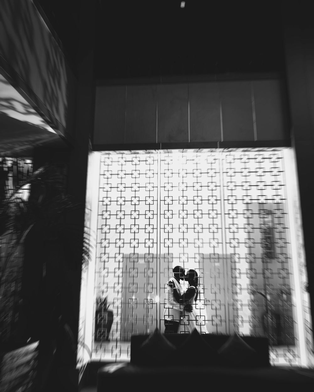 A silhouetted couple stands against a patterned wall in black and white, creating a romantic geometric composition.