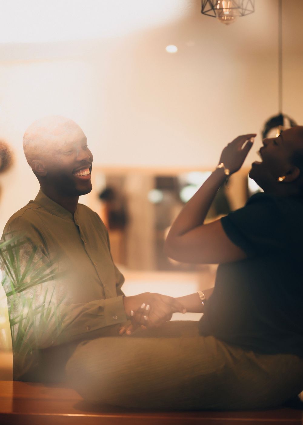 Two people share a joyful moment while sitting together in a warmly lit indoor setting.