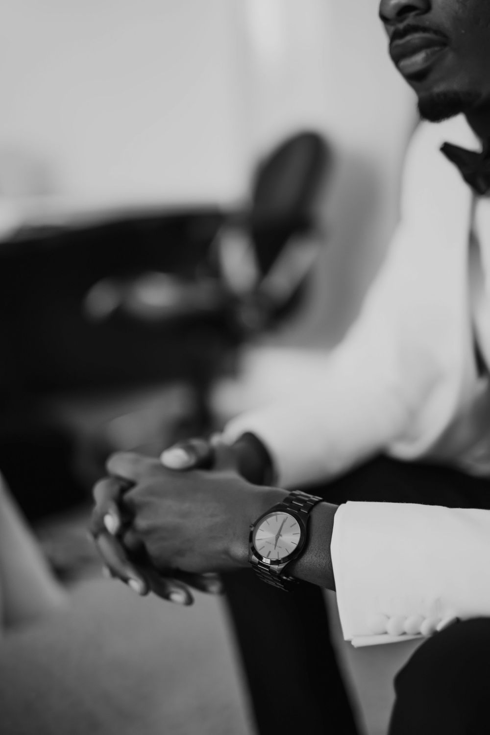 Black and white closeup of hands with a wristwatch while wearing formal business attire.