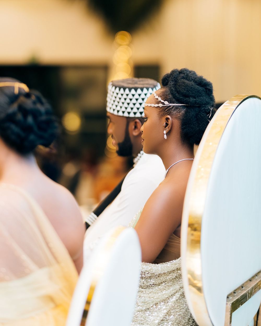 A couple sits together at their wedding reception wearing traditional formal attire including white and a kufi cap.