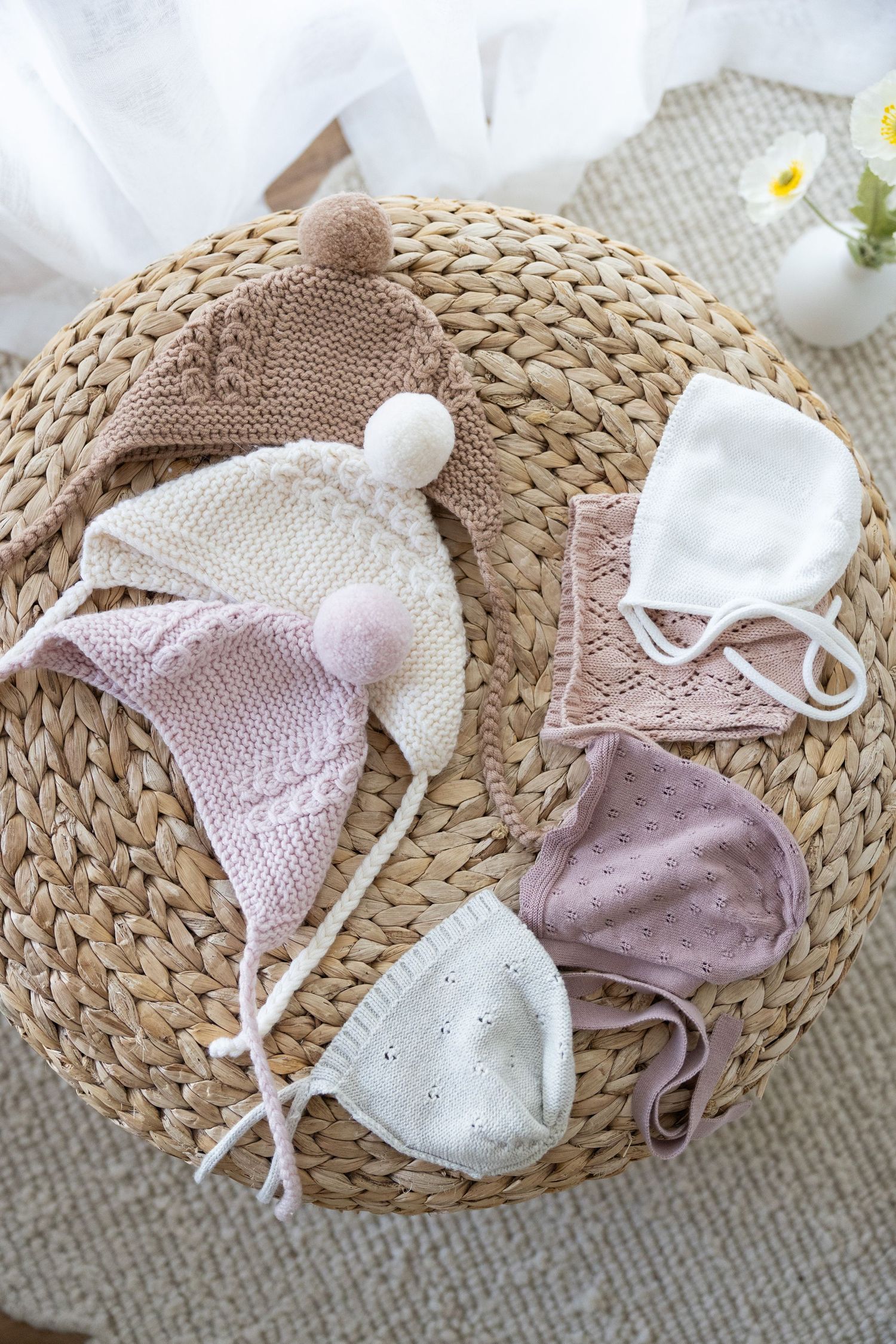 Collection of neutral and pastel baby accessories including bows, knit hats, and hair bands arranged on woven basket.