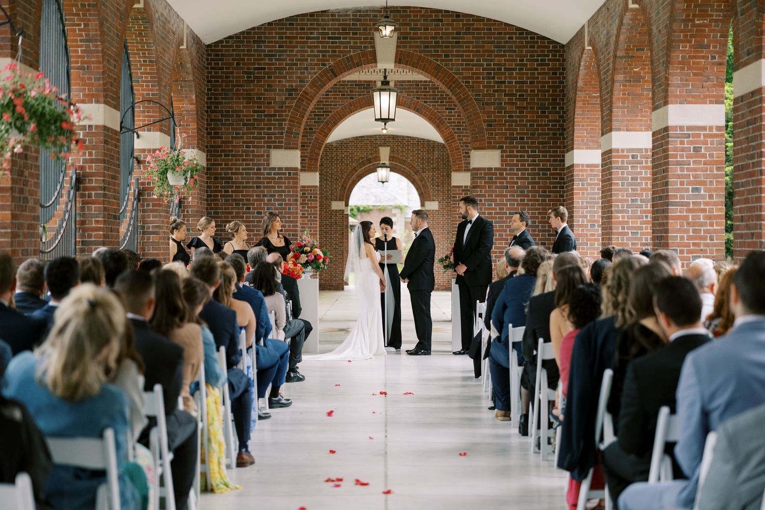 Wedding ceremony takes place in a brick archway with guests seated on both sides and rose petals lining the aisle at Hall of Springs.