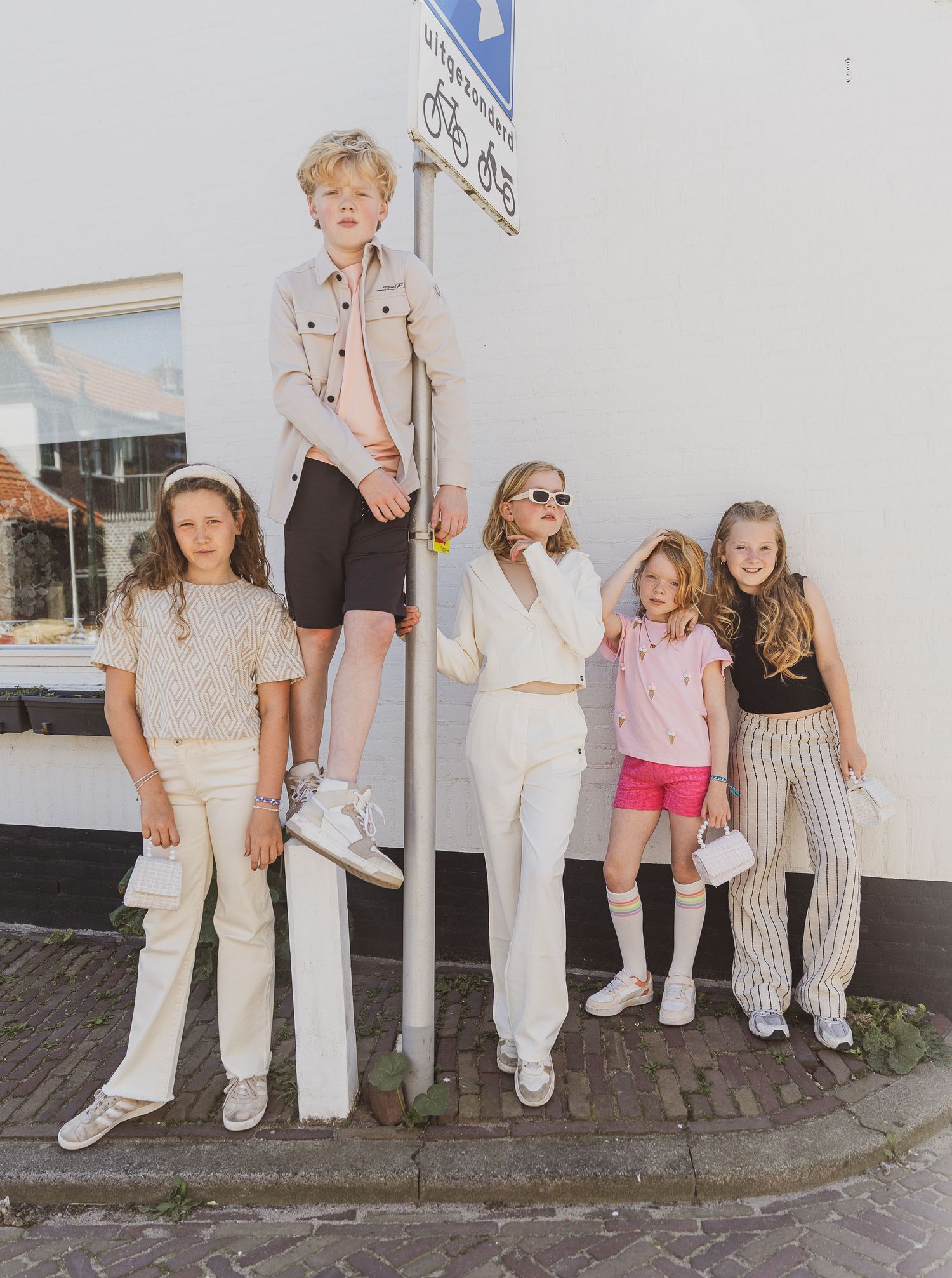A group in trendy casual outfits poses together against a white wall on a brick sidewalk. Humpy kinderkledingwinkel. Kinderkledingfotografie