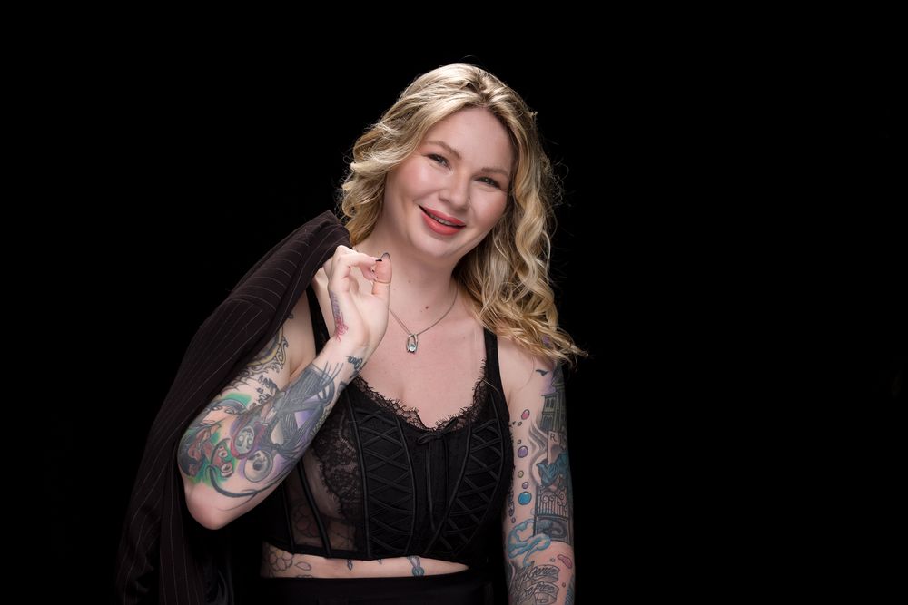 Glamour portrait with wavy blonde hair and black attire against dark backdrop.