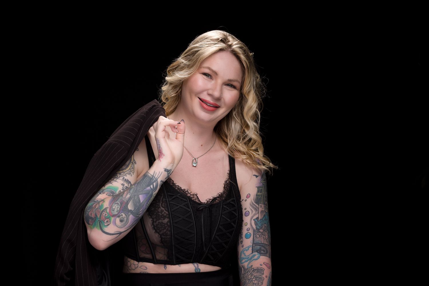 Glamour portrait with wavy blonde hair and black attire against dark backdrop.