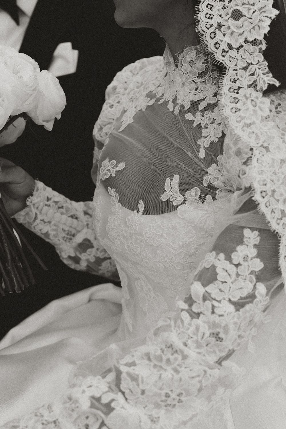 Close-up detail of a white lace wedding dress with intricate floral embroidery and delicate beading in black and white.