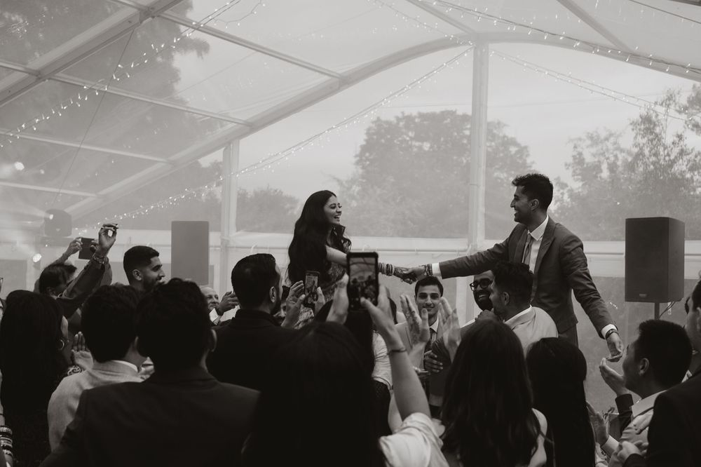 A black and white photograph of an energetic wedding reception with guests celebrating under a tented venue.