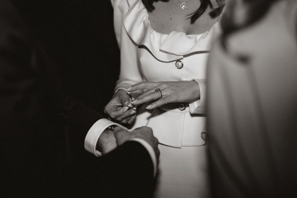 Black and white closeup of hands holding a ring during an intimate wedding ceremony moment.