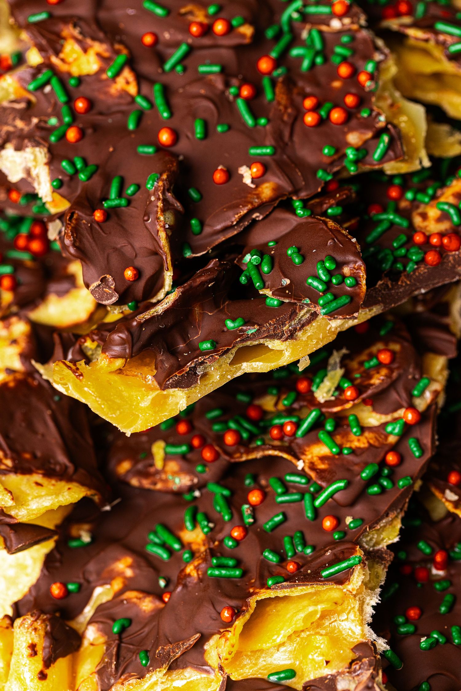 Stacked pieces of chocolate-covered toffee bark topped with festive green and orange holiday sprinkles.
