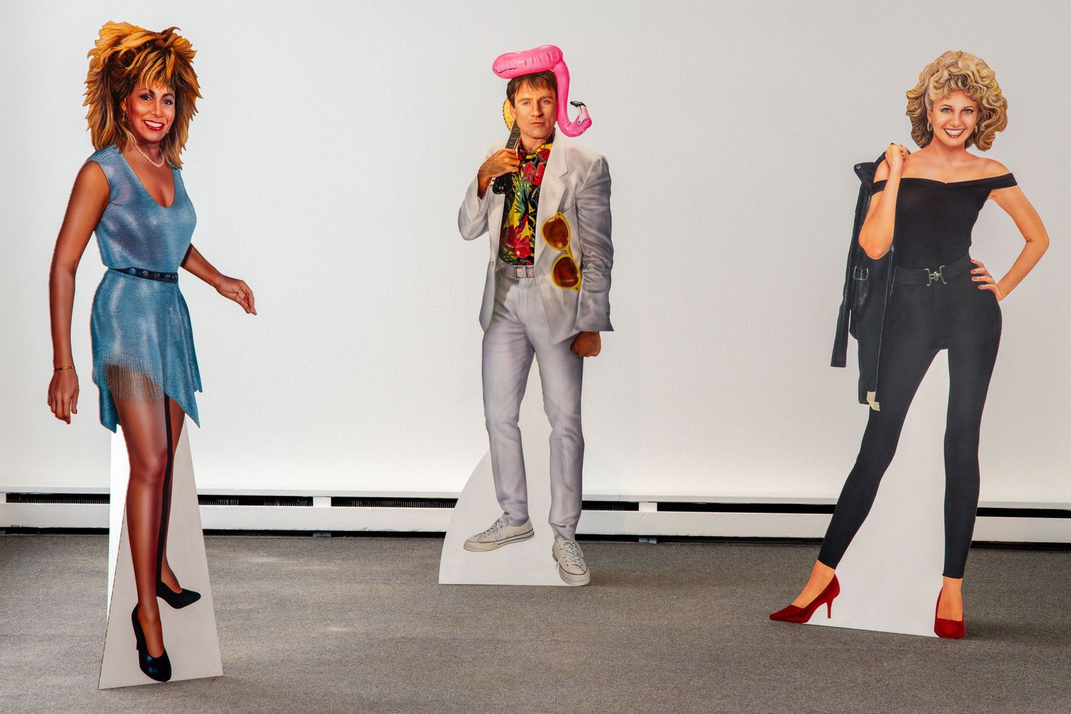 Life-sized cardboard cutouts of 1980s style fashion figures in colorful outfits against a white background.