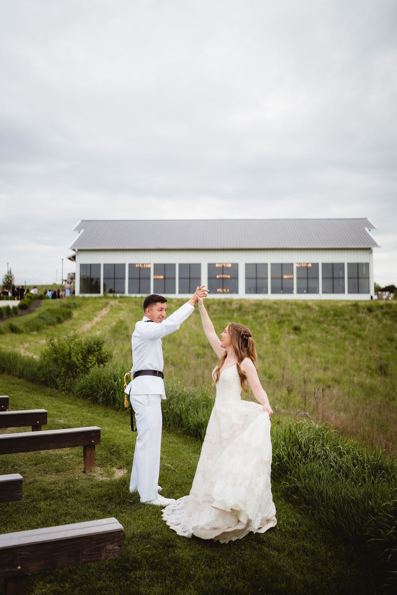 A couple dancing outdoors in wedding attire near a white building with large windows on a cloudy day.