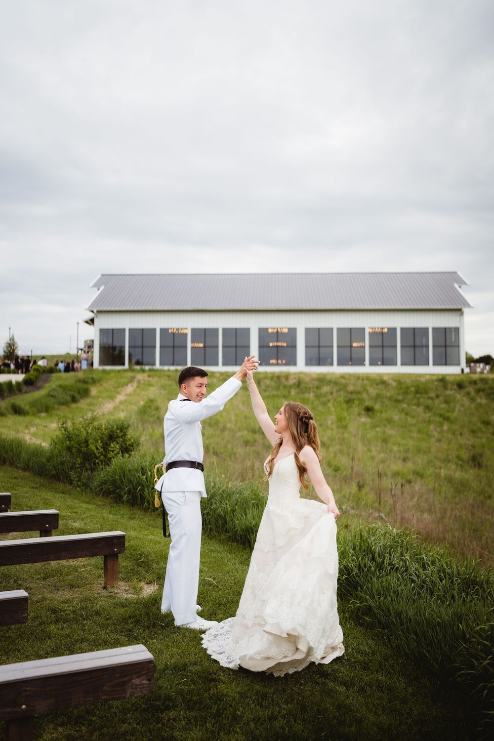 A couple dancing outdoors in wedding attire near a white building with large windows on a cloudy day.