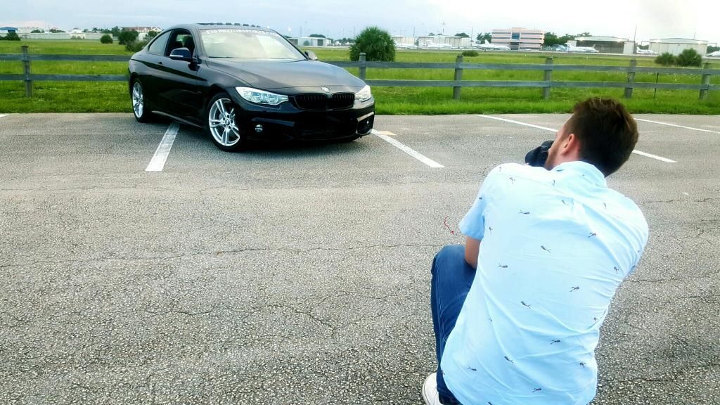 Photographer crouching to capture photo of black BMW in empty parking lot.