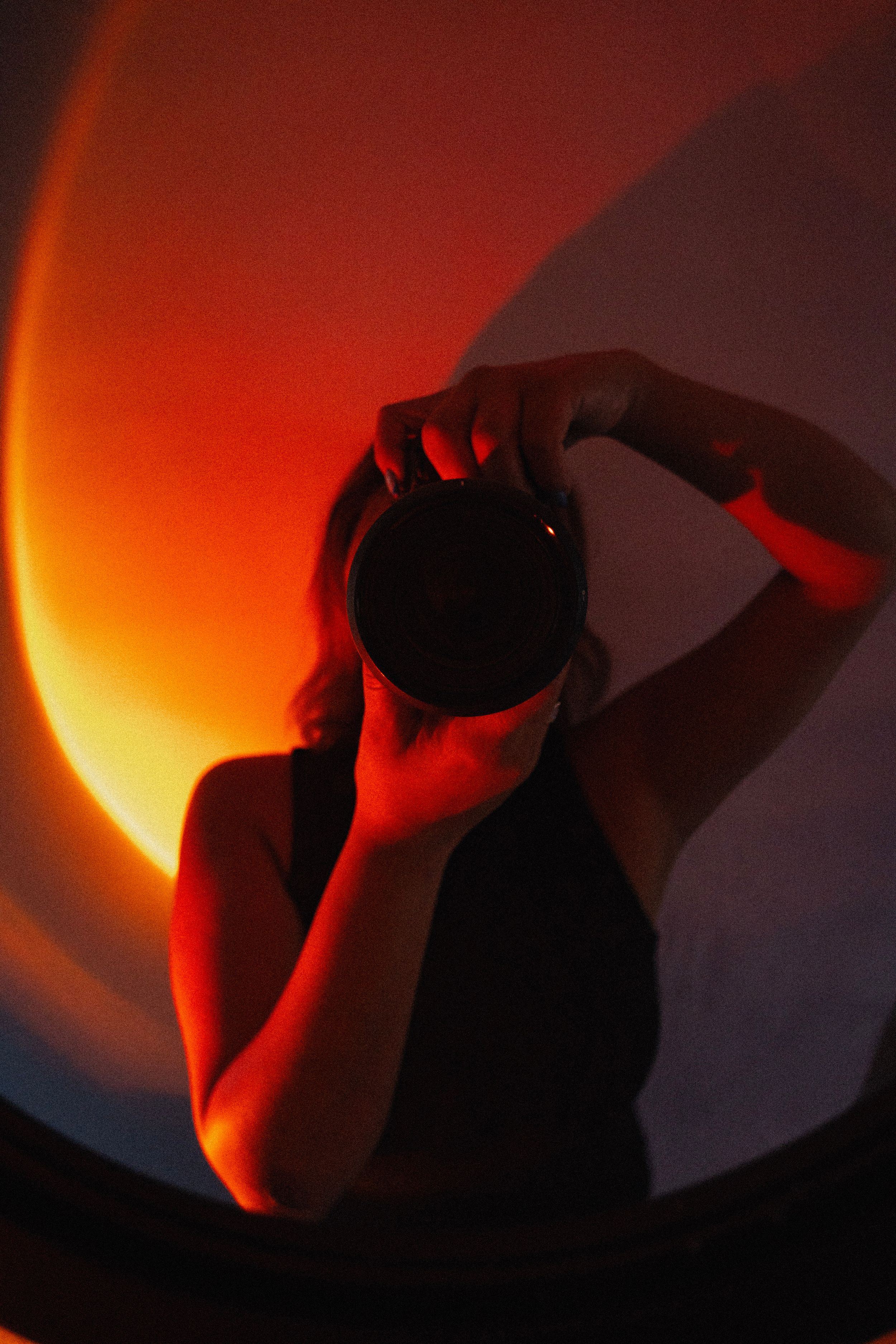 Silhouette taking a photo with a camera against a dramatic orange sunset glow in stylized lighting.